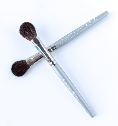 Two makeup brushes are shown with a round, bubble shaped application brush and with a gray handle inscribed with "La Bella Donna" and a metal ferrule.